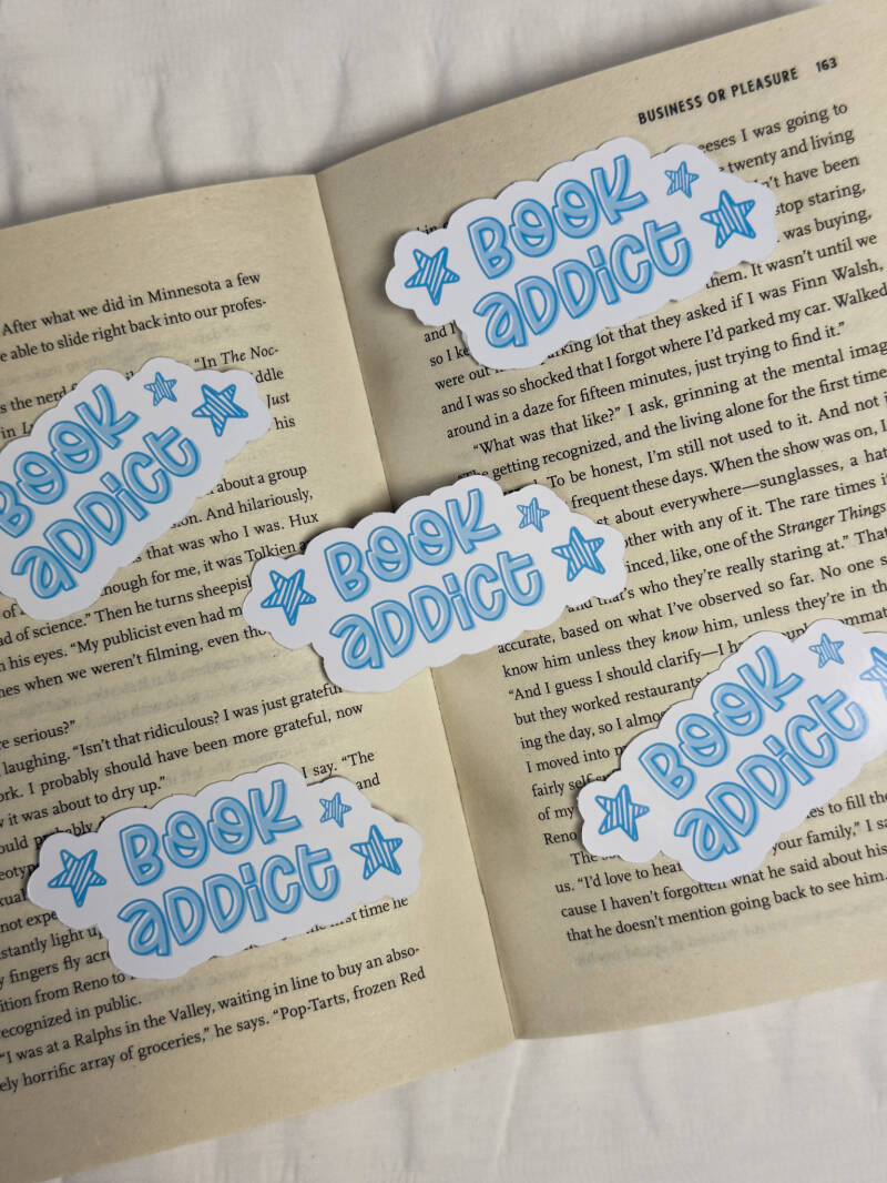 Boekenthema sticker met de woorden 'Book Addict' in blauw, omringd door kleine sterretjes, ideaal voor annoteren en bookish decoratie.