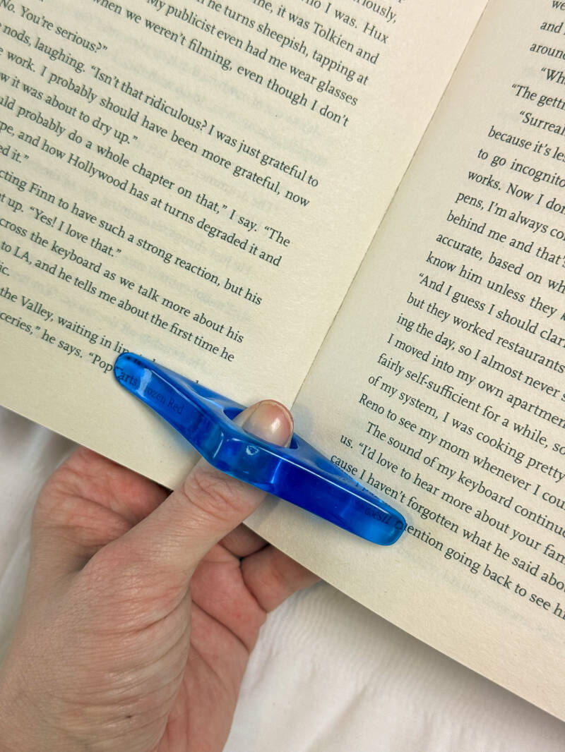 Blauwe duimring paginahouder op een open boek, ideaal om moeiteloos een boek open te houden tijdens het lezen.
