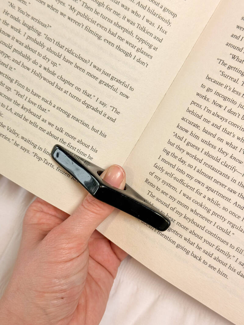 Een zwarte bladzijdehouder op een boek, ideaal om pagina’s open te houden tijdens het lezen.