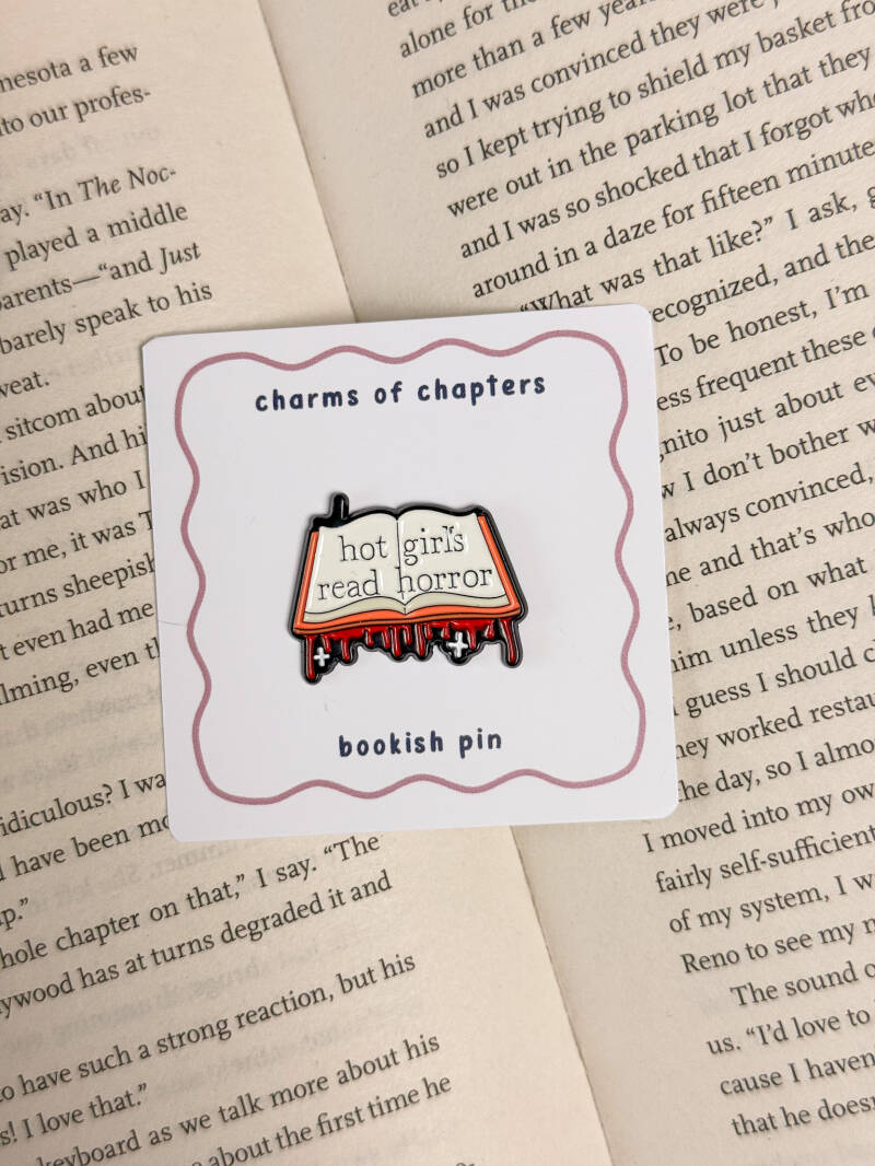 Enamel pin met een open boek en de tekst 'Hot girls read horror', met een bloederig horror-thema ontwerp.