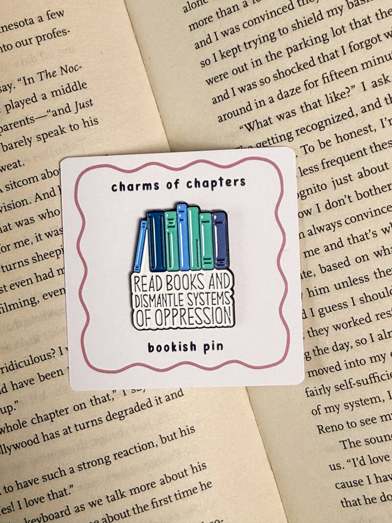 Enamel pin met een rij blauwe en groene boeken en de tekst: 'Read Books and Dismantle Systems of Oppression', ideaal voor boekenliefhebbers met een boodschap.