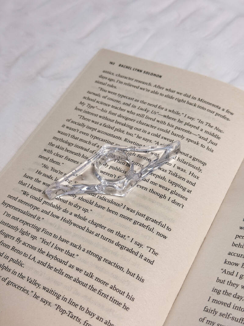 Transparante bladzijdehouder van Charms of Chapters, ontworpen om comfortabel te lezen met één hand.